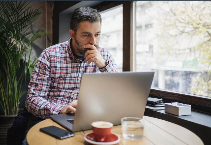 Un hombre revisa su laptop sentado junto a la ventana de un café